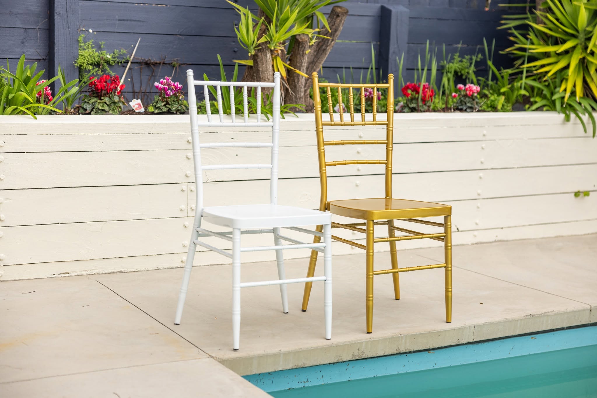 A white Chiavari chair and a gold Chiavari chair side by side at the edge of a swimming pool