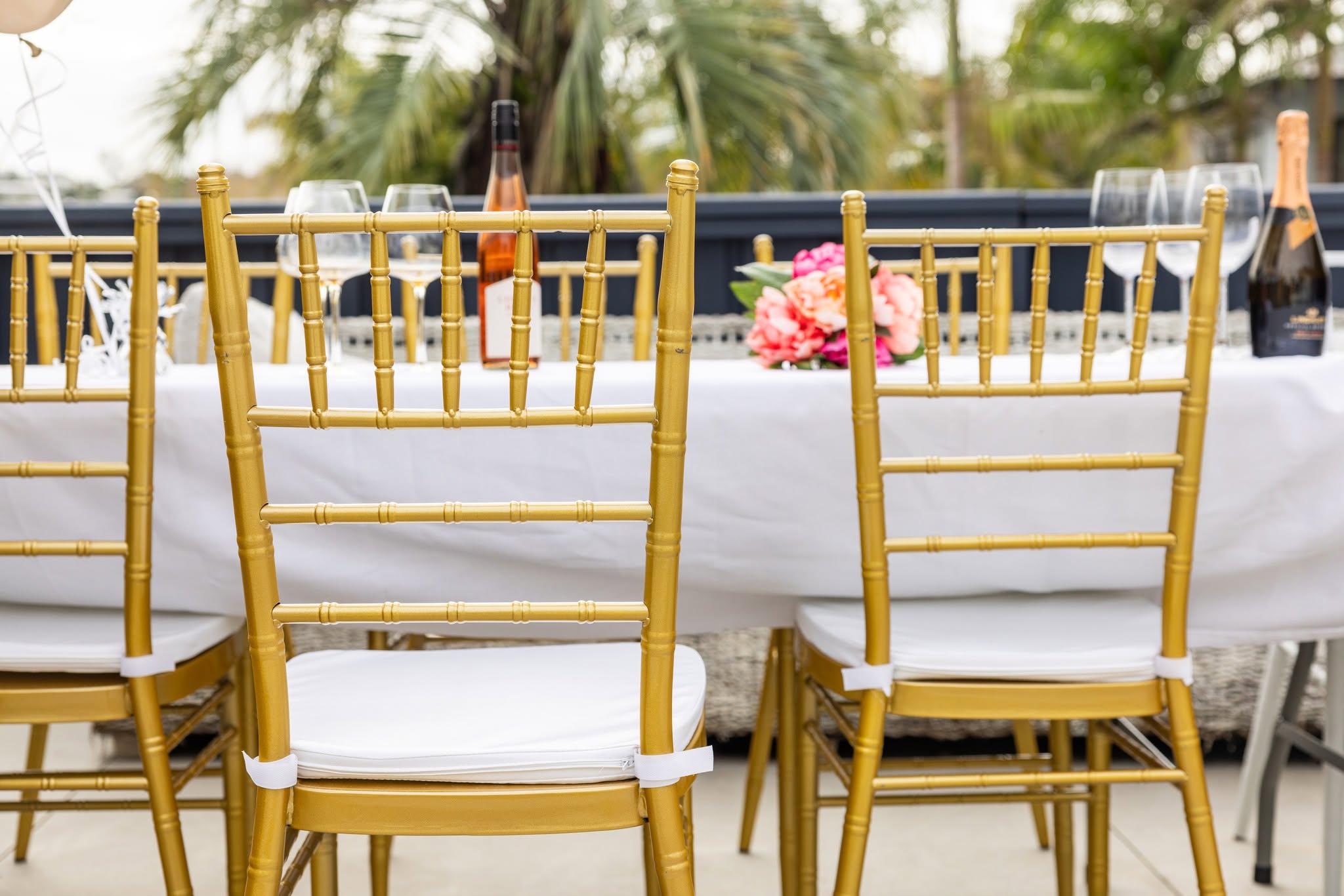 Gold Chiavari chairs pulled up to a white-clothed table set with wine, glasses and flowers